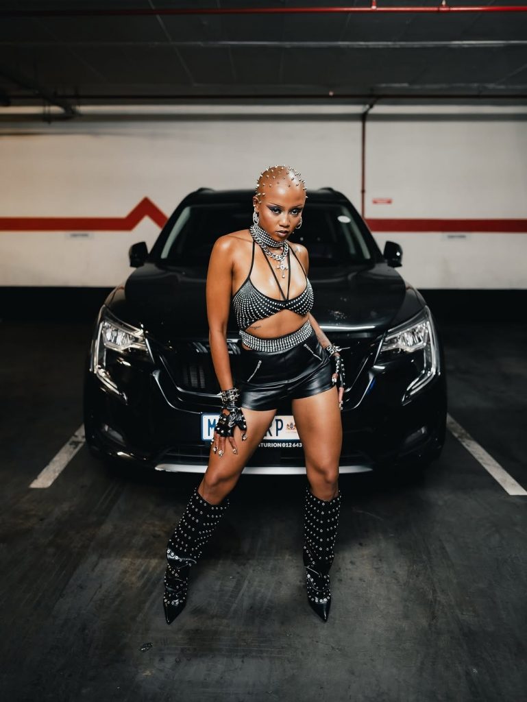 Moozlie commands attention in a black outfit with eye-catching silver thorn accents as she poses behind a black car. Picture: Instagram@Moozlie